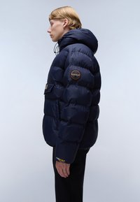 Giacca a vento blu navy con cappuccio, caratterizzata da un design trapuntato, una patch con logo sulla manica e un accento giallo "CORDURA" sul polsino.