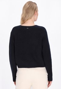 Laivastonsininen ribbiknit-neulepusero, jossa on pitkät hihat ja pyöreä kaula-aukko. Selässä on huomaamaton brändilogo. Lyhyt malli.