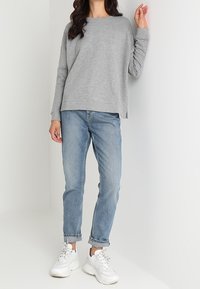 Grå sweatshirt med lös passform, rund halsringning och långa ärmar, kombinerad med ljusblå jeans och vita kraftiga sneakers.