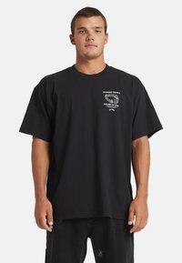 Black cotton t-shirt with a crew neck, short sleeves, featuring a white printed logo on the left chest area. Relaxed, loose fit design.