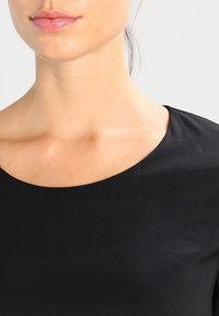 Mustapaita, jossa on leveä, pyöreä kaula-aukko, valmistettu sileästä kankaasta. Näyttää olkapäät ja kaulan alueen, pehmeällä ja tasaisella pinnalla. Minimalistinen muotoilu.