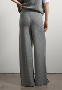 Pantaloni ampi grigi in maglina con una consistenza morbida, caratterizzati da una vita alta e una cintura elastica. Caviglie orlate con linee pulite.