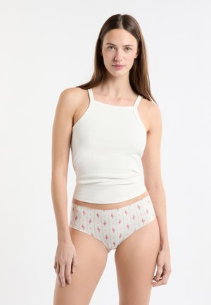 Weißes geripptes Tanktop mit schmalen Trägern, kombiniert mit beiger Unterwäsche mit Blumenmuster, die vertikale Streifen und kleine pinke Blumen zeigt.