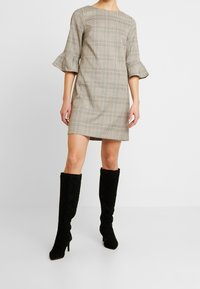 Rutig klänning i beige och bruna nyanser med utsvängda trekvartslånga ärmar, kombinerad med knähöga svarta mockastövlar.