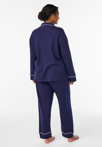 Navy blue pajama set made from soft fabric. Features long sleeves with white piping, relaxed fit pants, and a collared top.