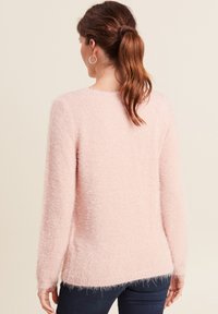 Flauschiger, hellrosa Pullover mit langen Ärmeln und lockerer Passform; besitzt eine weiche Textur und einen leicht geschwungenen Saum auf der Rückseite.