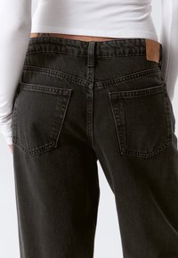 Jean en denim noir avec taille haute et jambes effilées. Présente deux poches arrière et un patch en cuir à la taille.
