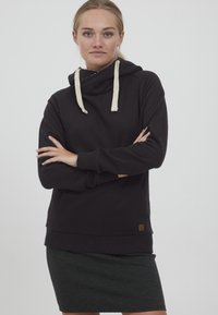 Sudadera negra con capucha ajustable, que presenta acentos en beige y un bolsillo tipo canguro. El material parece suave con puños de canalé.