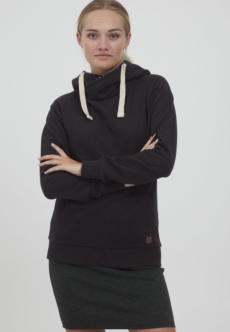 Sudadera negra con capucha ajustable, que presenta acentos en beige y un bolsillo tipo canguro. El material parece suave con puños de canalé.