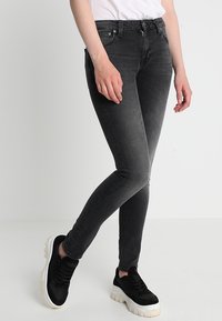 Svarta slim-fit jeans med blekning, fem fickor och dragkedja. Bärs med svarta sneakers med vit sula.