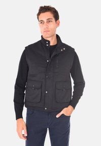 Gilet nero realizzato in tessuto testurizzato con colletto alto, zip frontale e bottoni a pressione. Presenta due tasche frontali e cuciture dettagliate.