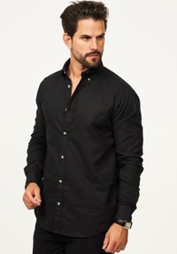 Schwarzes Langarmhemd mit Button-Down-Kragen, weißen Knöpfen und taillierter Passform. Hergestellt aus weichem, strukturiertem Stoff mit glatter Oberfläche.