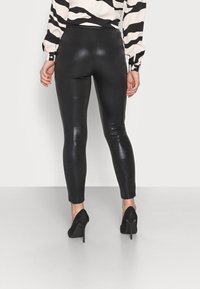 Svarta, kroppsnära leggings av glänsande material, med hög midja och ankel-lång design, kombinerade med svarta högklackade skor.