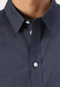 Camicia button-up blu navy con colletto, realizzata in un tessuto testurizzato e dotata di due bottoni davanti. Design pulito senza fantasie.