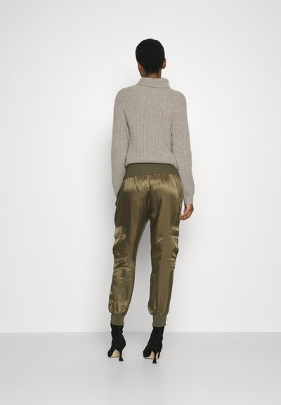 Light grey ribbed sweater with a high collar, paired with olive green satin cargo pants featuring pockets and fitted cuffs. Black heels complete the look.
