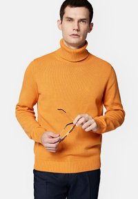 Sweter typu golf w jaskrawym pomarańczowym tricotowym materiale, z prążkowanym dołem i mankietami. Model trzyma okulary przeciwsłoneczne, prezentując luźny krój.
