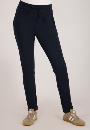 Marineblauwe joggers van rekbare stof, voorzien van een tailleband met trekkoord, een slim fit en enkelboorden. Gecombineerd met grijze sneakers.