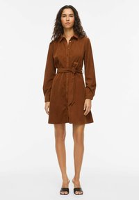 Robe-chemise en velours côtelé marron avec boutons, manches longues et ceinture nouée à la taille. Dotée d'un col et d'un ourlet à hauteur du genou.