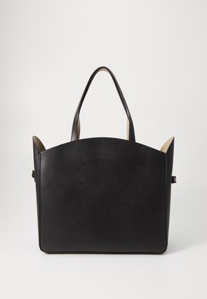 Sac cabas en cuir noir avec deux poignées et un logo circulaire perforé sur le devant, sur un fond blanc uni.