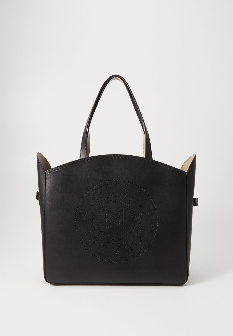 Sac cabas en cuir noir avec deux poignées et un logo circulaire perforé sur le devant, sur un fond blanc uni.