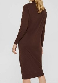 Robe en maille marron avec un col montant, des manches longues et des poignets côtelés. Le modèle présente une silhouette ajustée et un ourlet à hauteur des genoux.