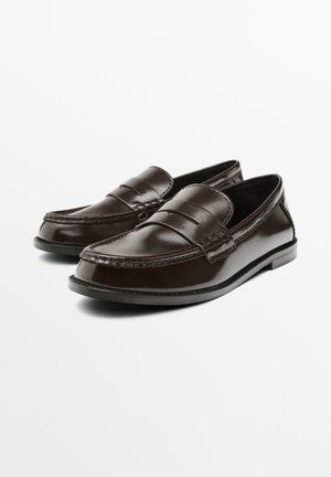 Braune Lederloafers mit einer glatten Oberfläche, einem gesteppten Obermaterial und einem erhöhten dekorativen Riemen. Flache Sohle und rundes Zehendesign.