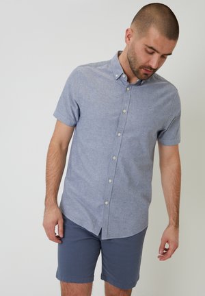 Korte mouwen overhemd met knoopsluiting in lichtblauwe stof, voorzien van een kraag en een gladde textuur. Gecombineerd met donkerblauwe shorts.