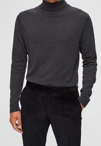 Mörkgrå turtlenecktröja med långa ärmar, ribbad hals och mudd, i kombination med svarta kordbyxor med flat front.