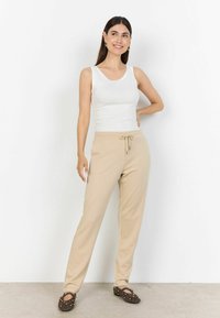 Beżowe spodnie dresowe ze ściągaczem w talii, w połączeniu z dopasowanym białym topem na ramiączkach. Spodnie mają gładką fakturę i luźny krój.