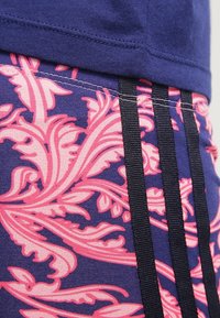 Námořnický vršek z látky s květinovým růžovým vzorem, doplněný černými vertikálními pruhy. Má hladkou texturu a kontrastní barevnou kombinaci.