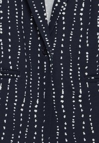 Blazer marine avec rayures verticales blanches en pointillé, fermeture simple par un bouton noir et deux poches avant passepoilées.