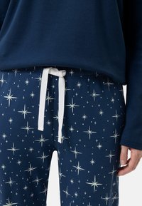 Marineblå pyjamas sæt med en langærmet top og bukser med stjernemønster. Bukserne har en hvid snøre og spredte stjernedesign.