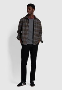 Gestapeltes Outfit mit einem grauen karierte Flanellhemd über einem grauen T-Shirt, kombiniert mit schwarzen Hosen und schwarzen Sneakers mit weißen Streifen.