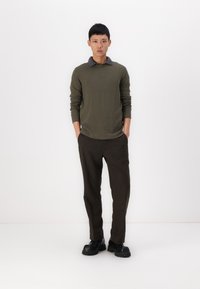 Cămașă lungă de culoare verde militar cu guler gri, asortată cu pantaloni îngustați de culoare maro închis și încălțăminte chunky neagră. Material texturat.