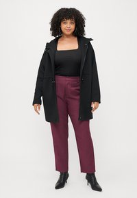 Veste à capuche noire, à manches longues, fermeture éclair, associée à un pantalon bordeaux, coupe slim, tissu texturé, et bottines.