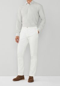 Camicia a maniche lunghe grigio chiaro con colletto, pantaloni bianchi su misura e scarpe in suede marroni con lacci. Design semplice con un dettaglio a bottoni sul colletto.