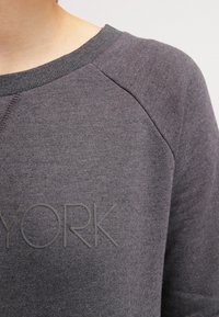 Felpa grigia realizzata in materiale morbido, con colletto rotondo, maniche raglan e testo in rilievo "YORK" sul davanti.