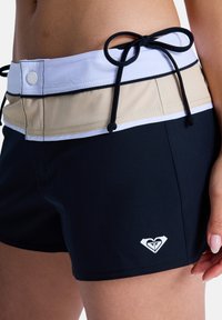 Shorts de bain noirs avec une ceinture beige et blanche. Comprend une fermeture à cordon et un petit logo blanc sur le côté gauche.