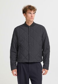 Giacca nera imbottita con colletto a coste, chiusura a bottoni a pressione e tasche laterali. Il design presenta un motivo strutturato e una vestibilità dritta.