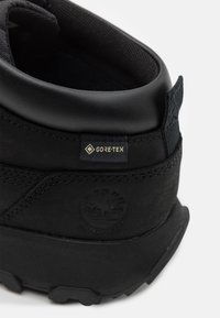 Černá nepromokavá turistická bota s patou, na níž je štítek z tkaniny Gore-Tex a vyražené logo stromu na texturovaném okraji podrážky.