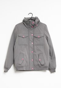 Giacca grigia con colletto alto, bottoni a pressione rosa, due tasche sul petto e due tasche laterali. Il materiale appare liscio con una texture leggermente lucida.