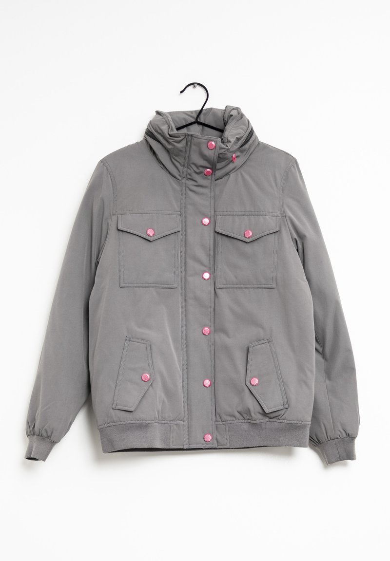 Giacca grigia con colletto alto, bottoni a pressione rosa, due tasche sul petto e due tasche laterali. Il materiale appare liscio con una texture leggermente lucida.