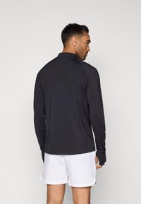 Μαύρη αθλητική μπλούζα με μακριά μανίκια και εφαρμοστή σχεδίαση, που διαθέτει ψηλό γιακά και άψογη κατασκευή στους ώμους. Συνδυασμένη με άσπρη βερμούδα.