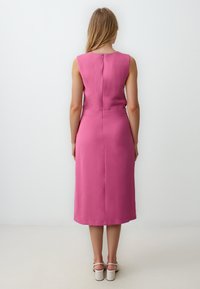 Ärmelloses, midi-langes Kleid aus leuchtend pinkem Stoff, mit einem taillierten Oberteil und einem geraden Rock. Mit einem Reißverschlussverschluss im Rücken.