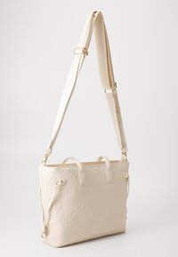 Sac fourre-tout beige avec des motifs floraux et de logo en relief, doté de doubles anses supérieures et d'une bandoulière réglable pour des options de transport polyvalentes.