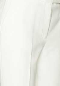 Pantaloni bianchi su misura con una texture liscia, dotati di una tasca laterale e un design a gamba dritta, che mettono in evidenza linee pulite e uno stile minimale.