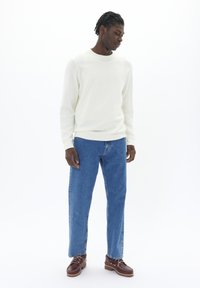 Balta vilnas kreklu džemperis ar zilu taisnu kāju džinsu un bordo krāsas šņorējamiem apaviem. Tīrs dizains, ikdienišķa piegriezne, minimālas tekstūras.