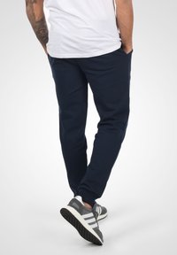 Marinblå joggers i mjukt tyg med en avsmalnande design, utrustade med sidofickor och ribbade muddar, kombinerade med grå sneakers.