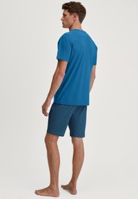 T-shirt en coton bleu associée à un short à motifs en marine, présentant un design géométrique. Style minimaliste avec une coupe décontractée.