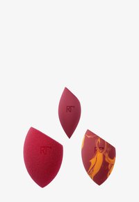 Tre spugnette per il trucco in tonalità di rosso. Una rossa uniforme, una rosso scuro con motivi marmorizzati arancioni e gialli, e una a forma di foglia appuntita.